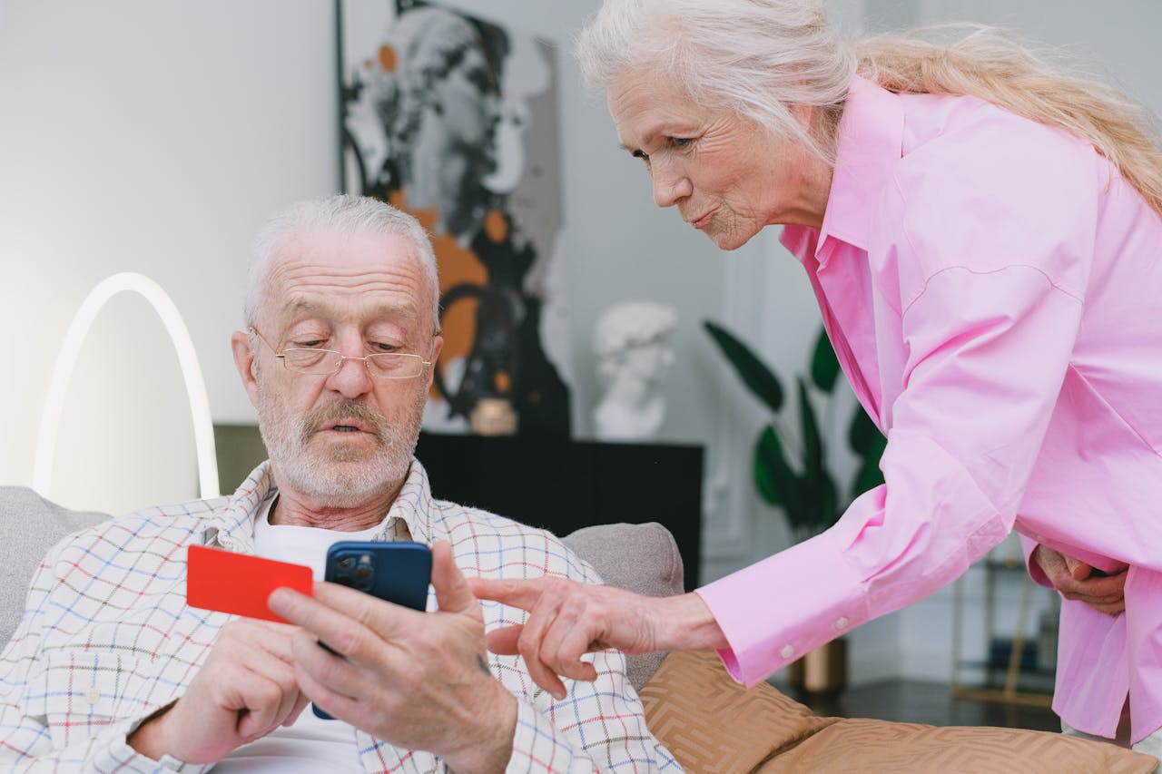 Elderly couple handling credit card transaction on smartphone indoors.